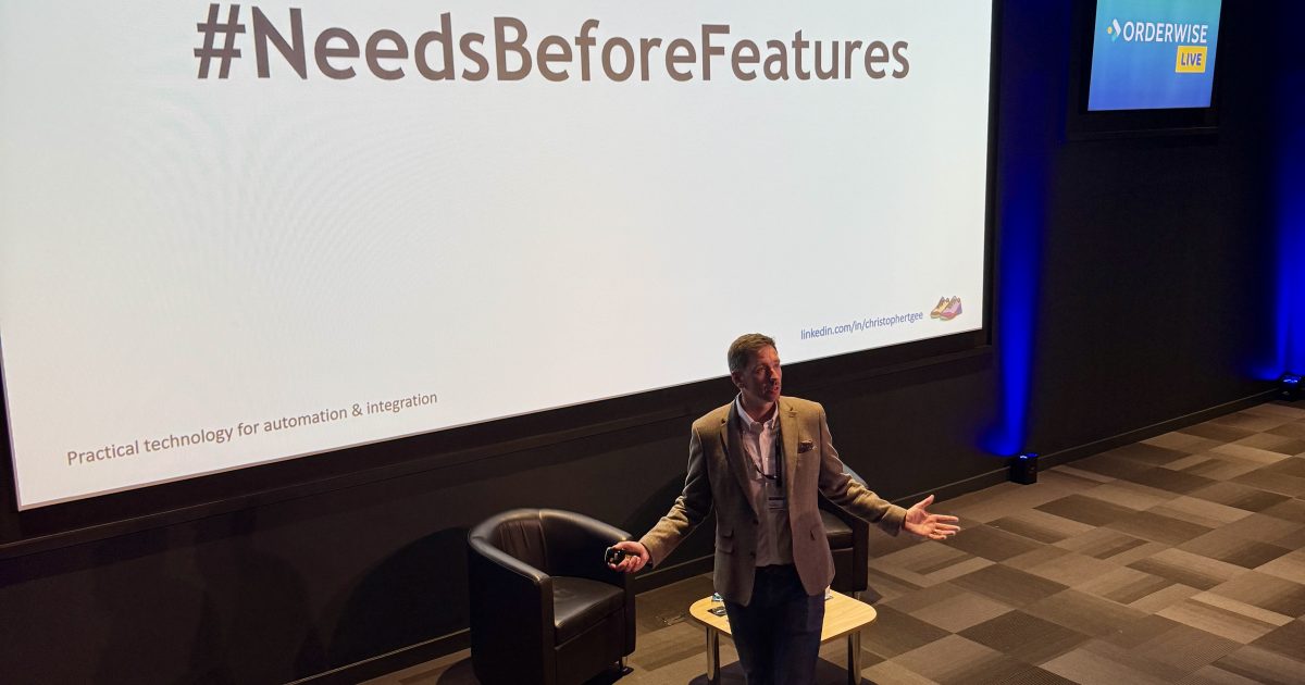 Speaker on stage discussing #NeedsBeforeFeatures at Orderwise Live conference.